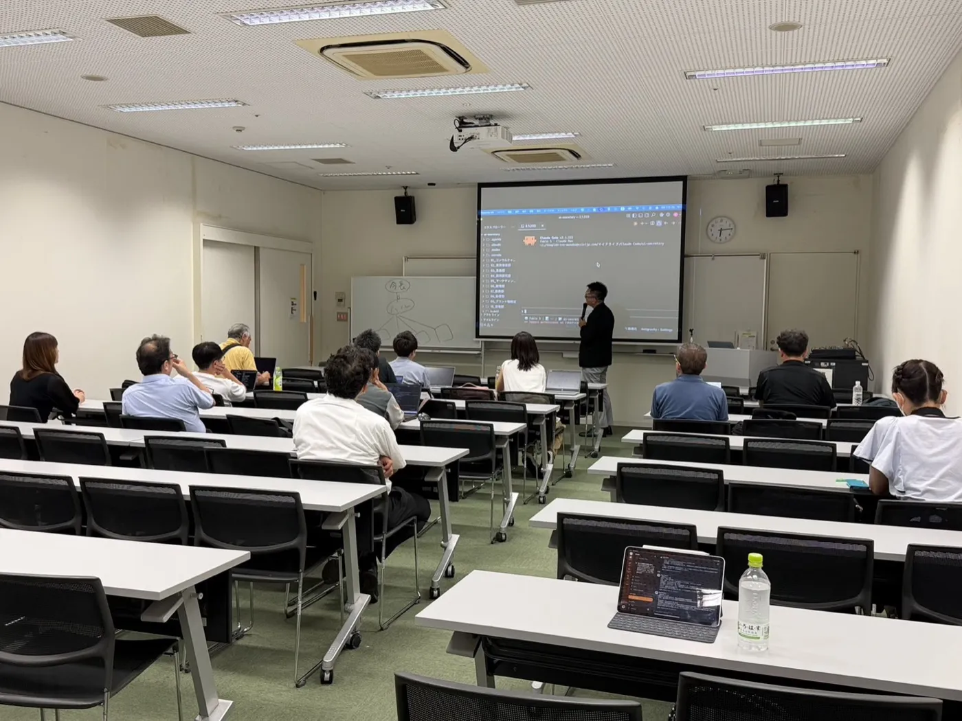 会場全体の様子。前方のスクリーンにはClaude Codeの操作画面が大きく映し出され、手前の机にはiPadが置かれています