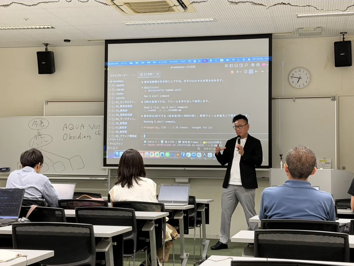 講師が身振りを交えて説明している様子。背後のスクリーンにはClaude Codeの画面が映っています