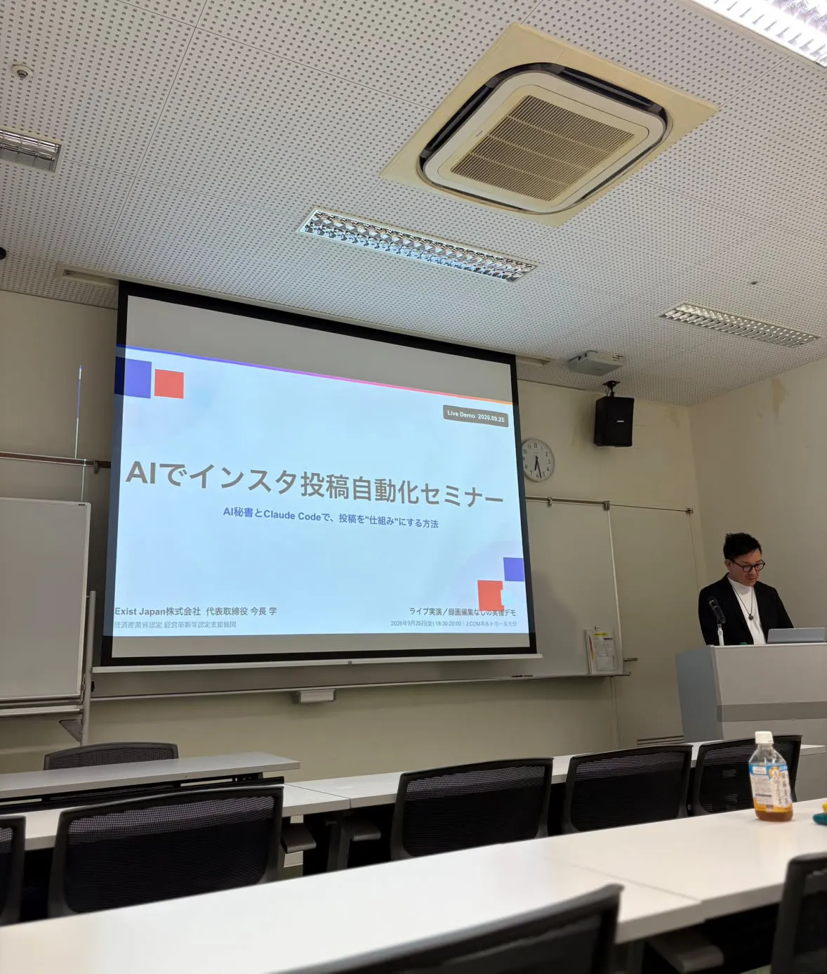 スクリーンに「AIでインスタ投稿自動化セミナー　AI秘書とClaude Codeで、投稿を"仕組み"にする方法」と映し、演台に立つ今長学